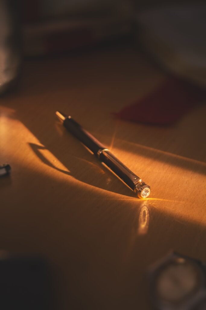 A luxurious pen rests on a sunlit wooden table, casting a gentle shadow.