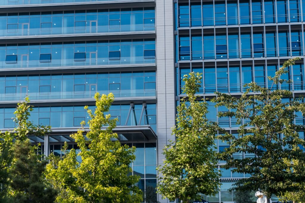 Contemporary glass office building facade with trees in front, reflecting urban environment.