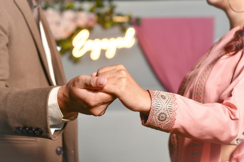 Close-up of couple's hands during an engagement, with 'Engaged' sign in background.