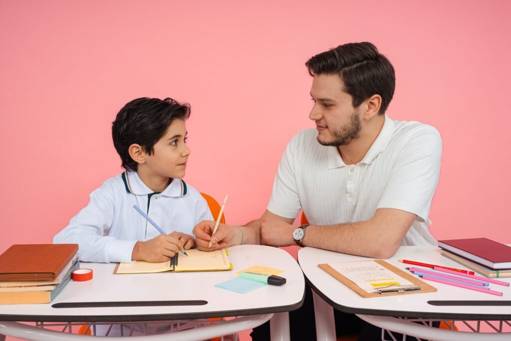 Father teaching his son at a desk with colorful stationery on a pink background.