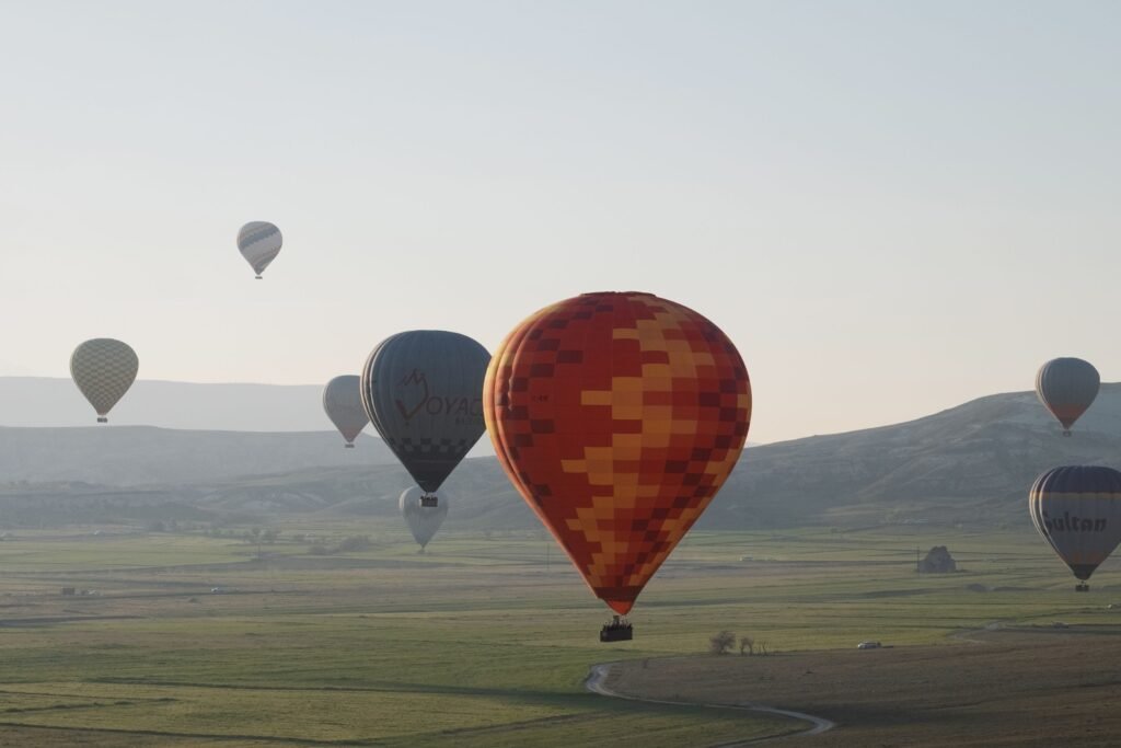 Colorful hot air balloons float above scenic Cappadocia landscape.