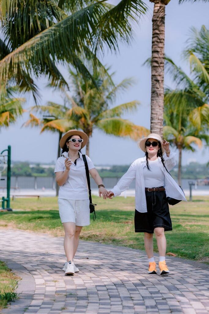 Two women enjoying a sunny walk in a lush tropical park holding hands.