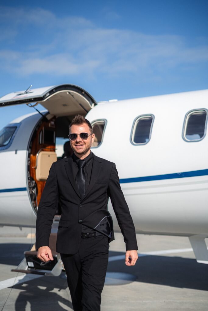 Confident businessman in a suit steps out of a private jet under a clear blue sky.