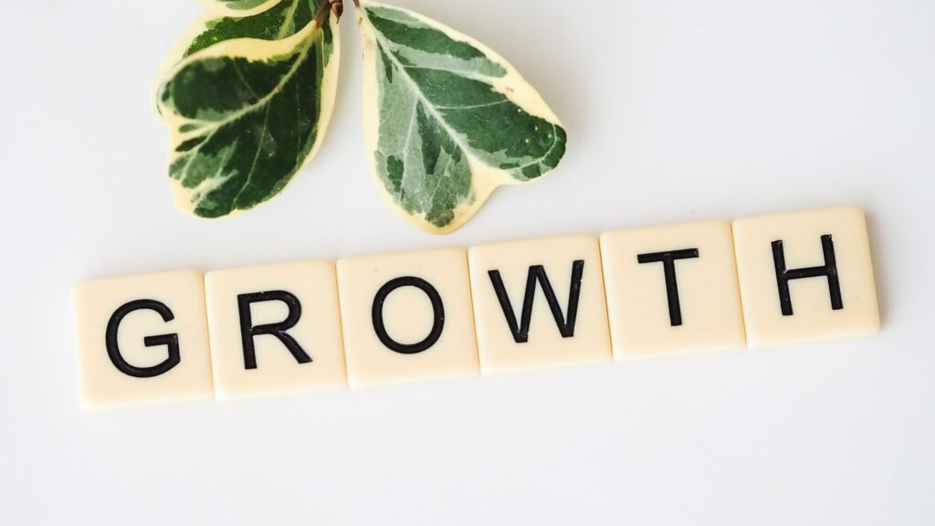 Close-up image of Scrabble tiles spelling 'Growth' with green leaves on a white background.
