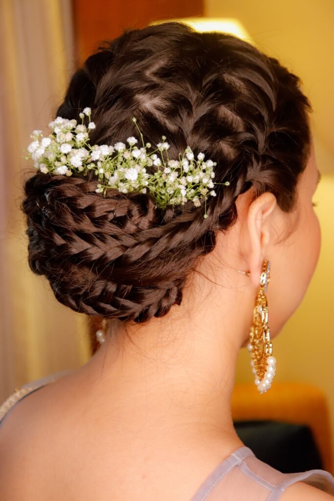 Back view of unrecognizable young female with elegant braided hairstyle decorated with gentle white flowers in festive attire standing in room